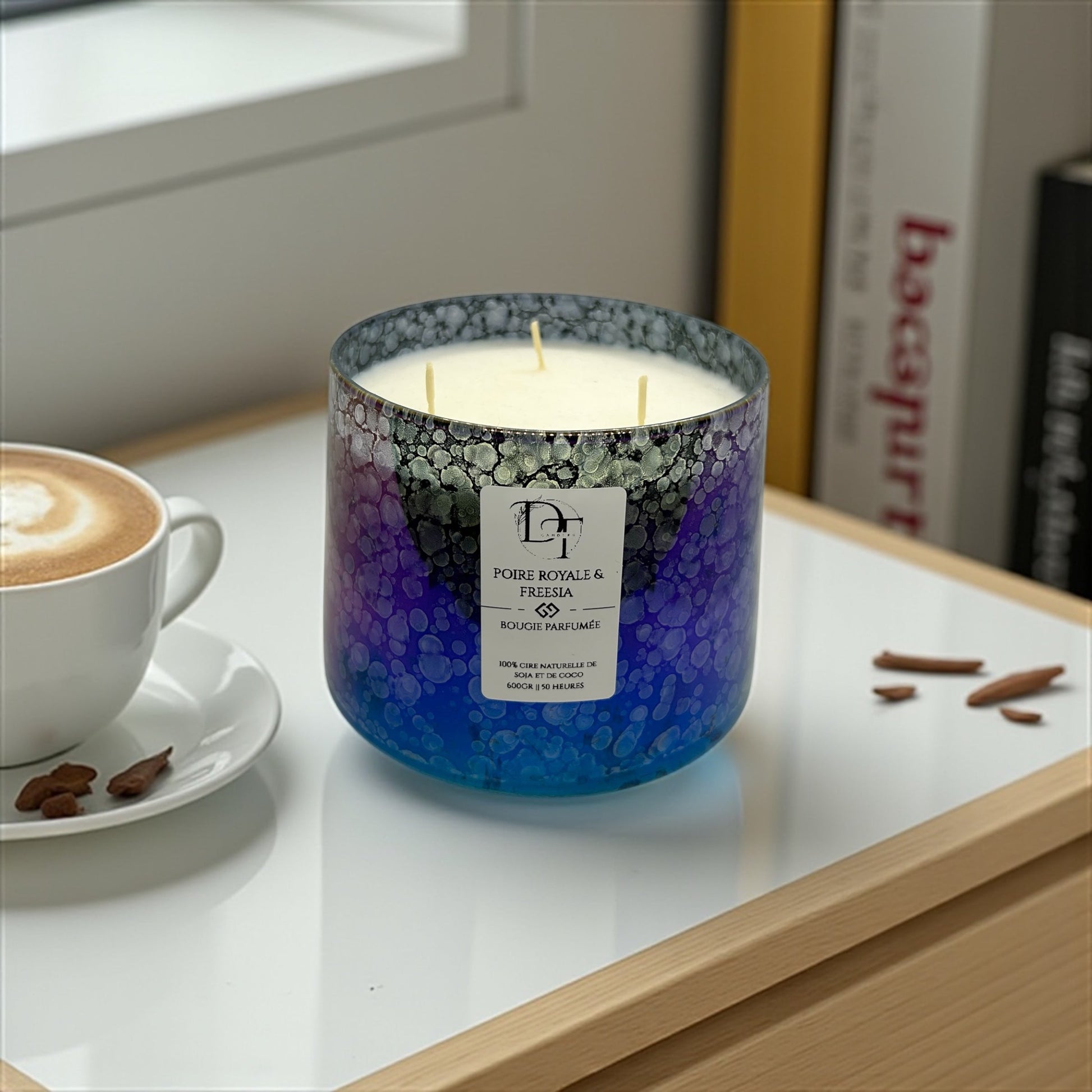 Candle with a gradient design on a table next to a cup of coffee