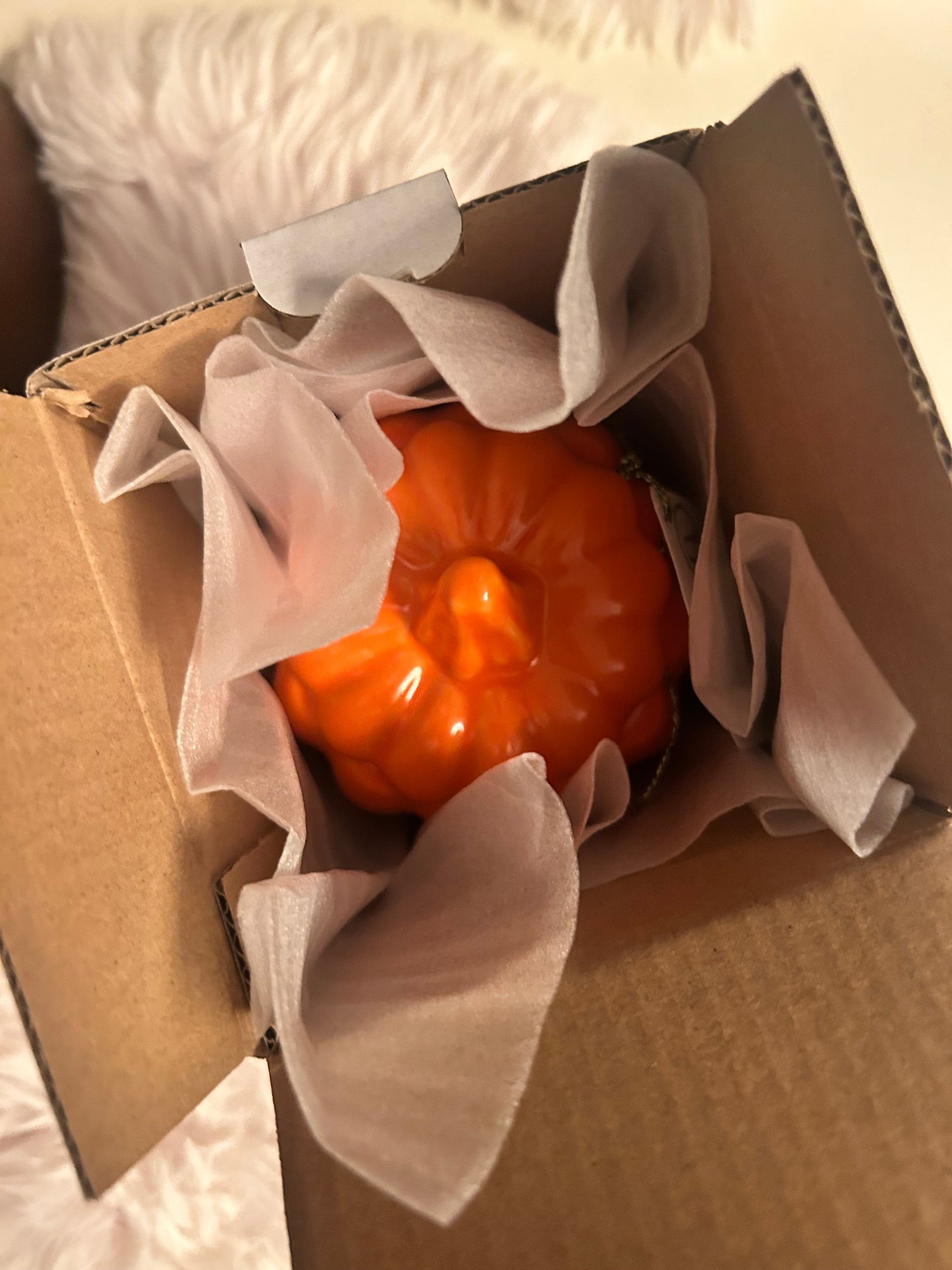 Small orange pumpkin candle inside a cardboard box with tissue paper