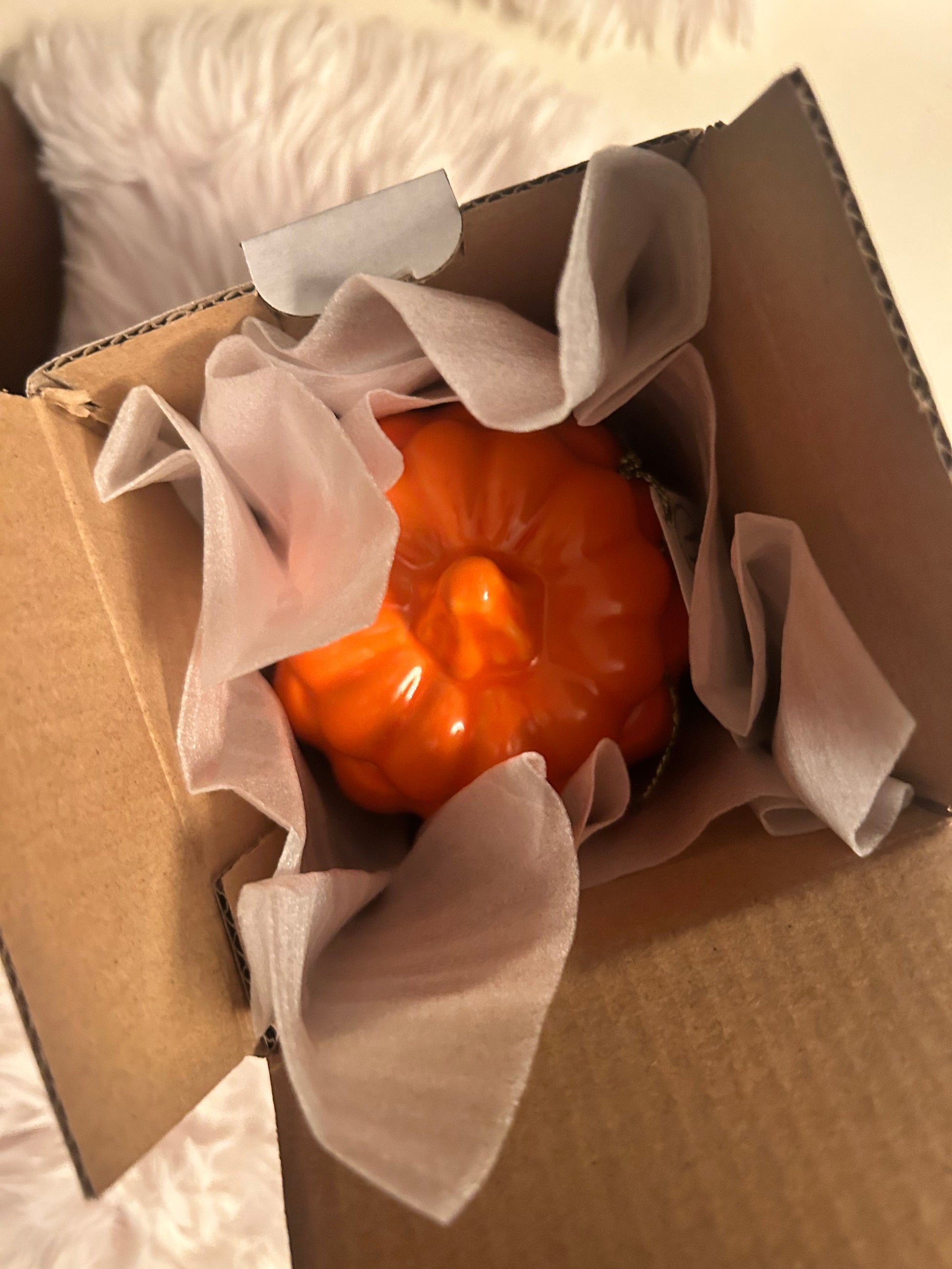Small orange pumpkin candle inside a cardboard box with tissue paper