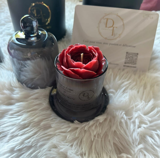 Red rose-shaped candle in a holder with a branded card on a fluffy white surface