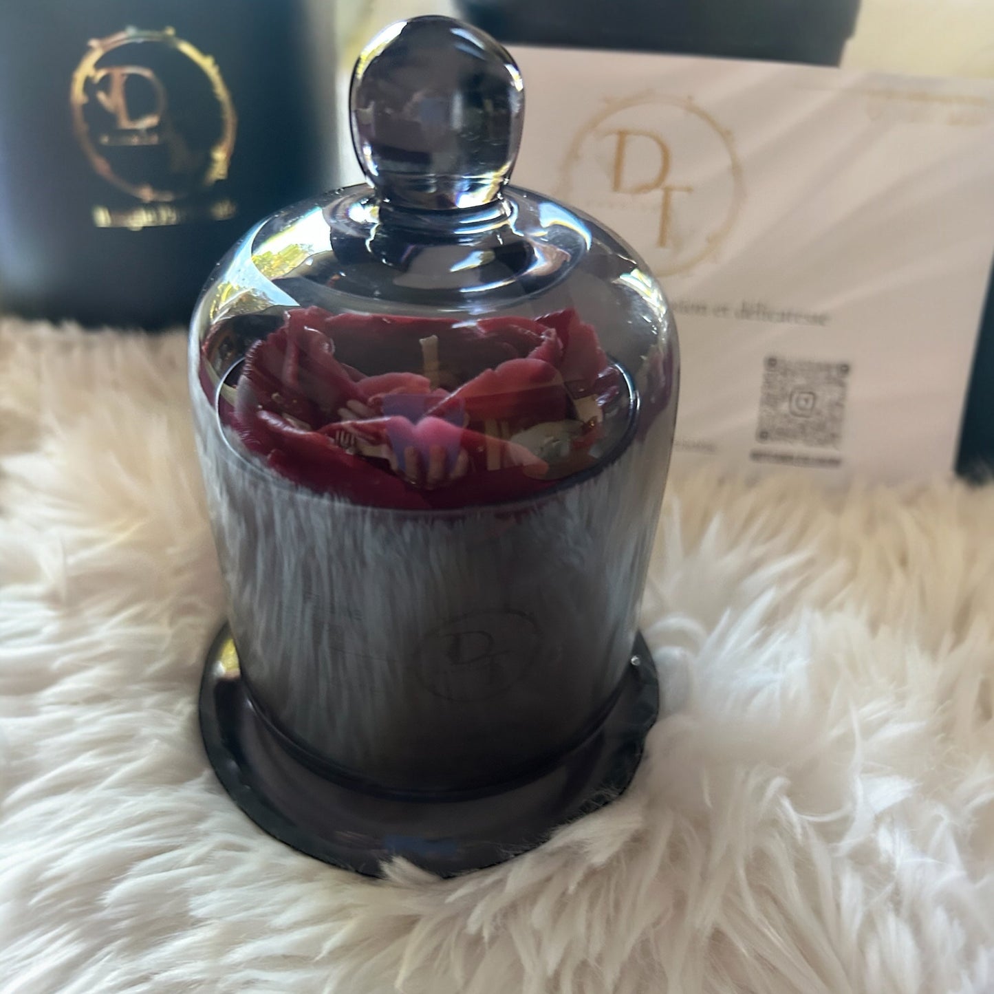 Decorative glass container with pink fabric inside, on a white fluffy surface with a branded box in the background.