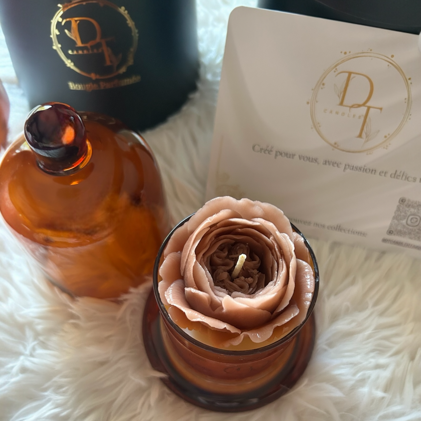 Rose-shaped candle with an amber bottle and branded card on a white surface