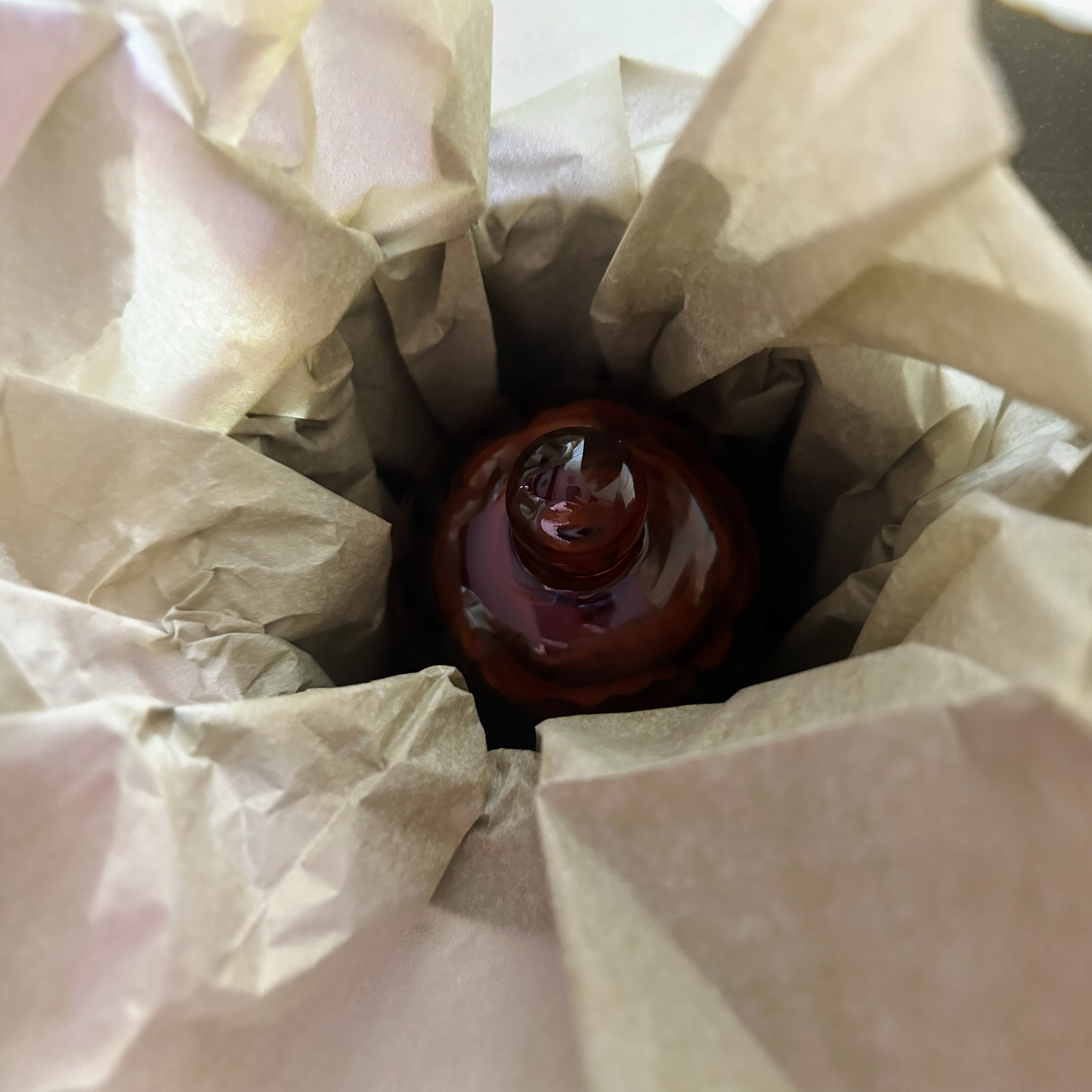 Red wine bottle wrapped in brown paper inside a white box