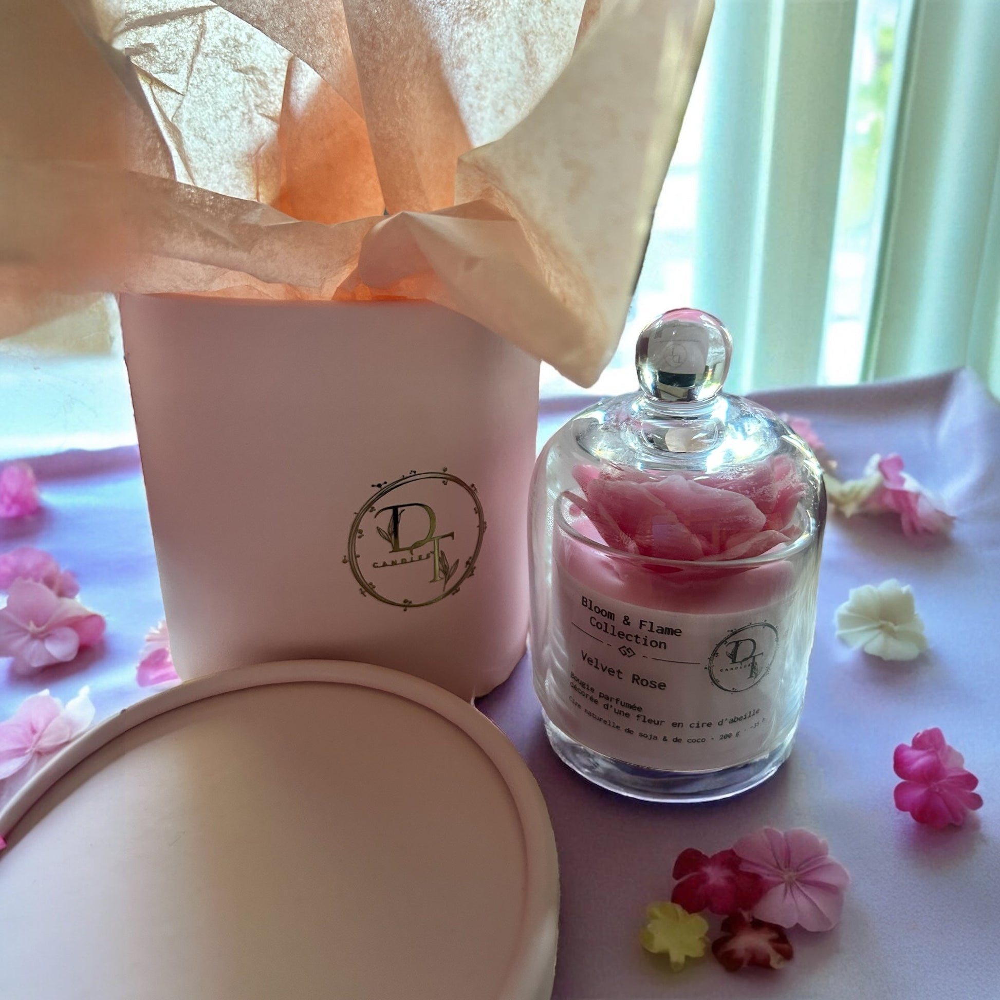 Perfume bottle with pink flowers and a pink box on a light purple surface with flowers.