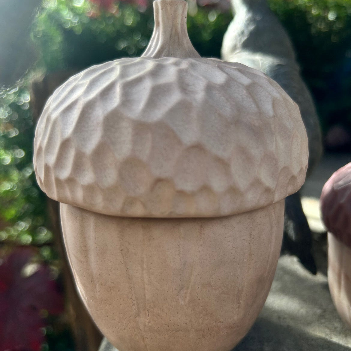Decorative stone acorn on a pedestal with blurred greenery in the background
