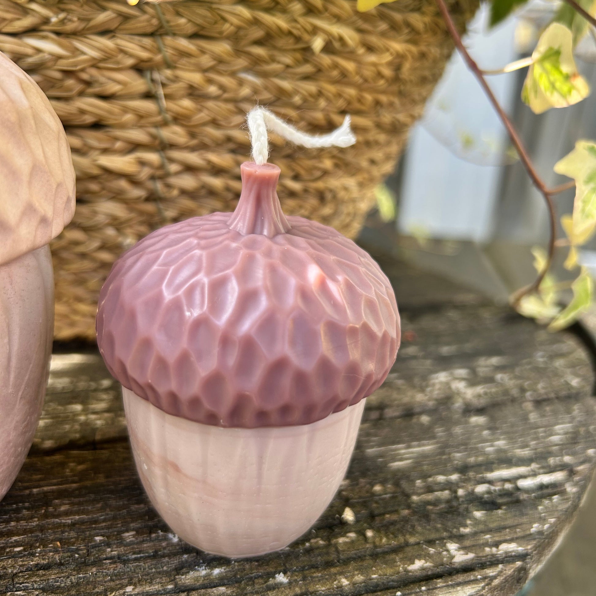 Pink acorn-shaped candle on a wooden surface with a woven basket in the background