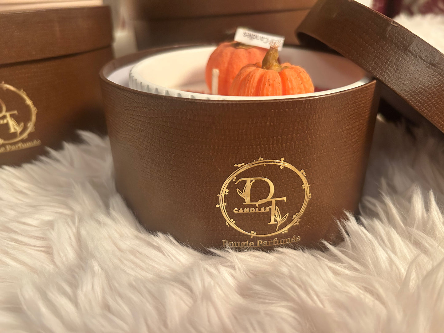 Brown candle in a decorative container with pumpkin decoration on a fluffy white surface
