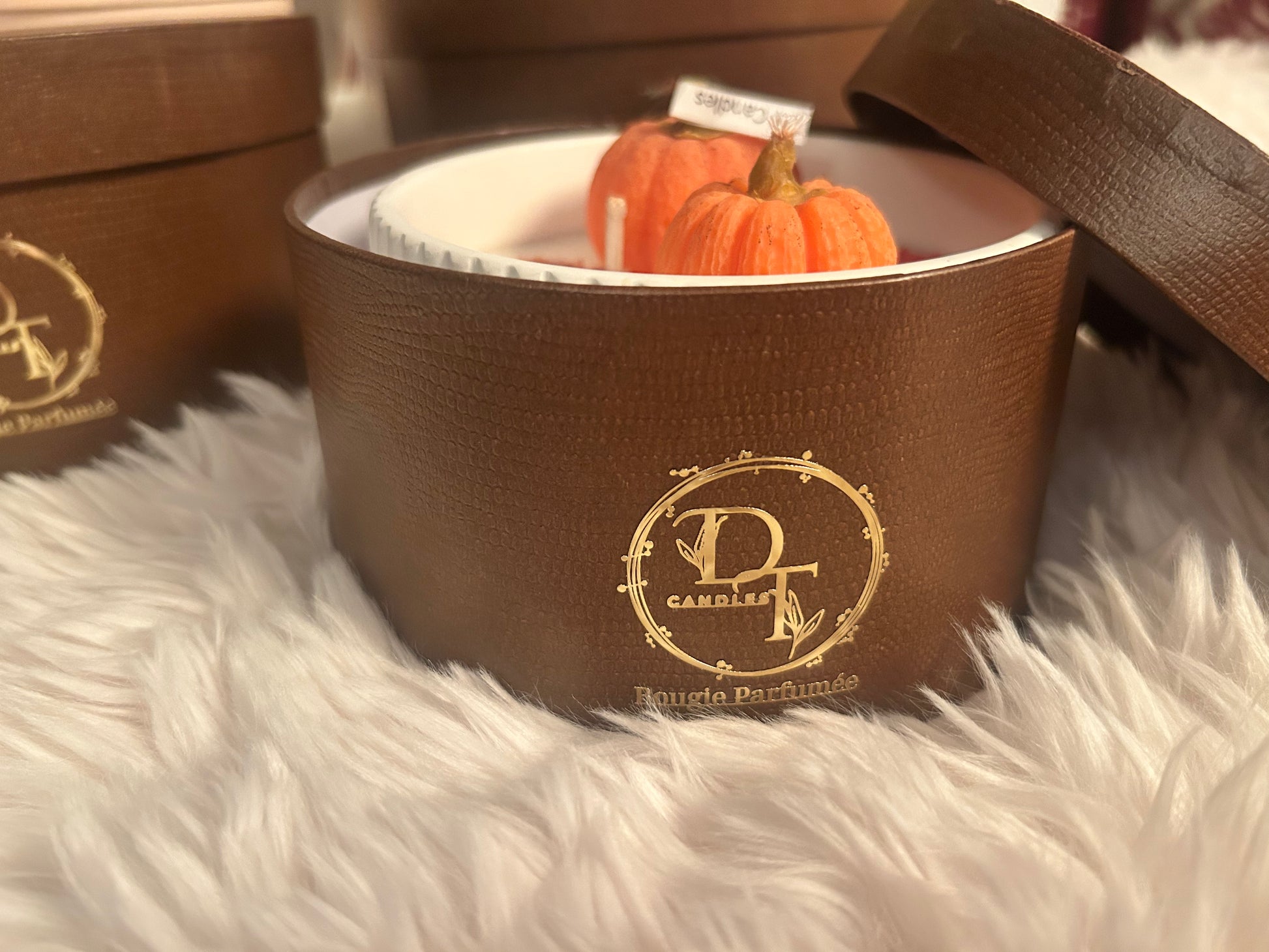 Brown candle in a decorative container with pumpkin decoration on a fluffy white surface